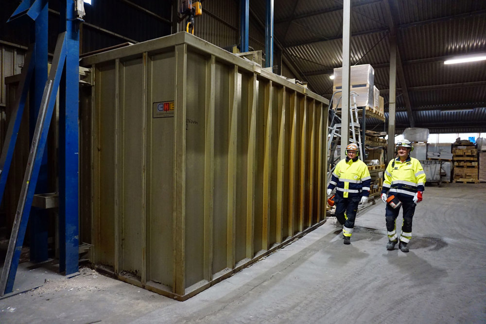 stor container, to menn går langs langsiden, innendørs