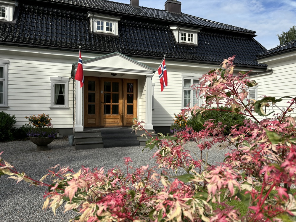 White house, norwegian flags at entrance, colourful bush in front