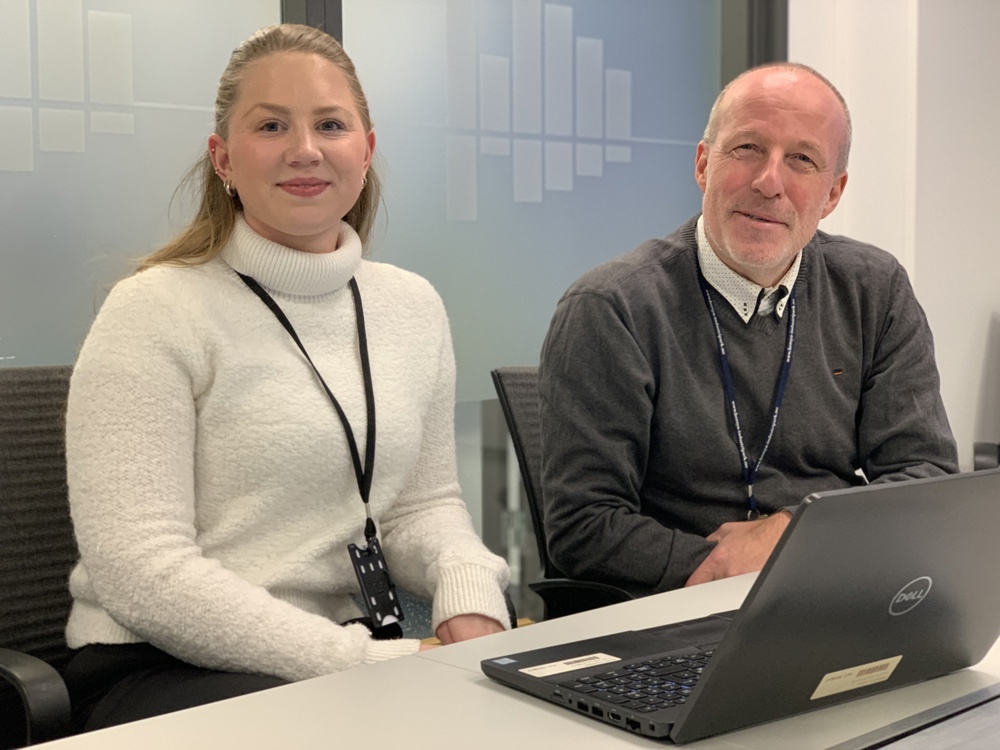 two persons sitting by a table, posing, laptop in front of them