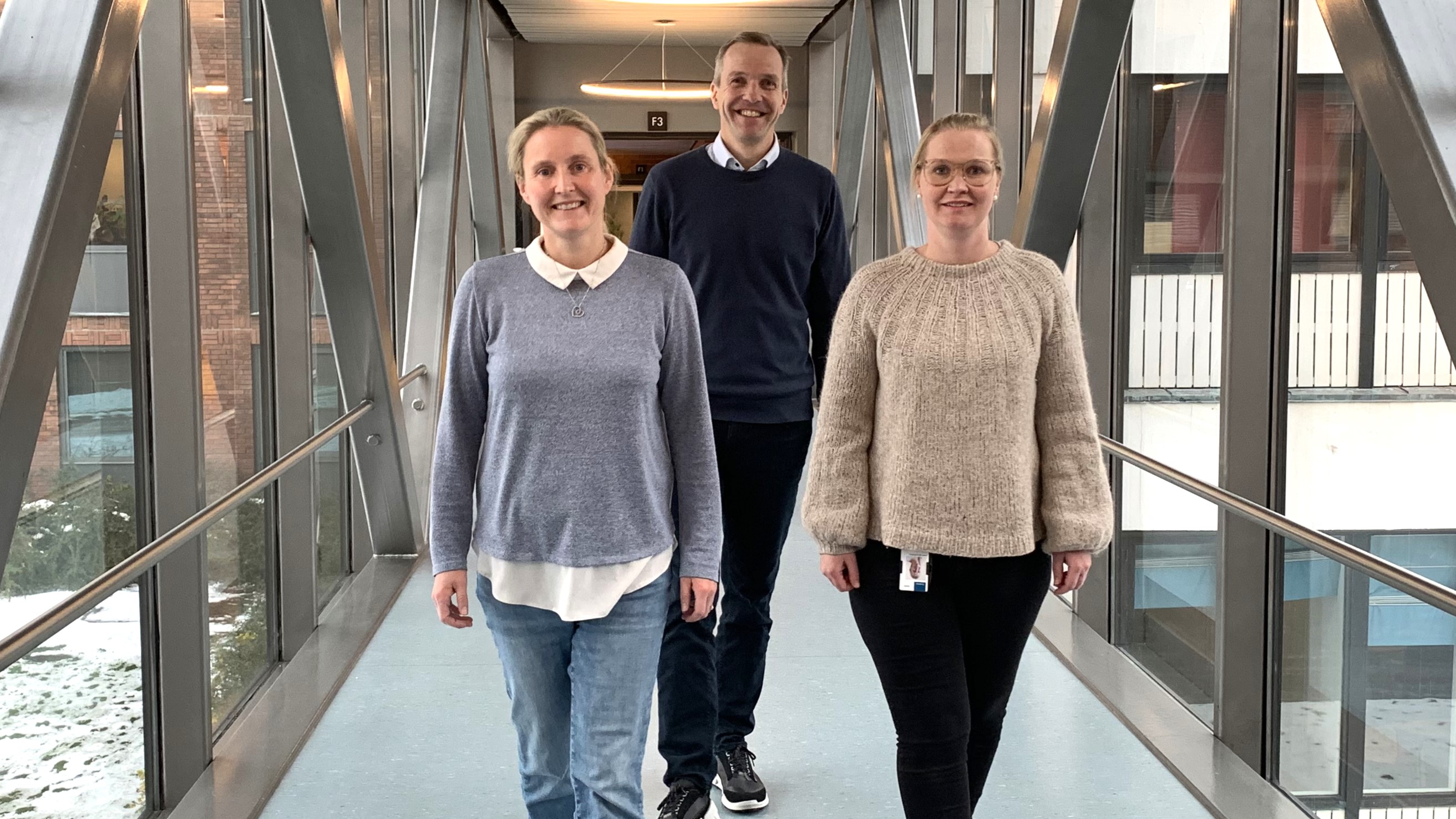 Three persons walking towards camera, posing, indoors, pedestian tunell with glass walls