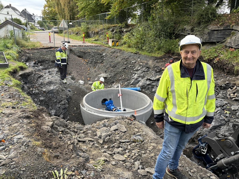 mann står foran stor grøft, i grøften monteres stor ventil i en sementring, to entreprenører i arbeidi grøften.