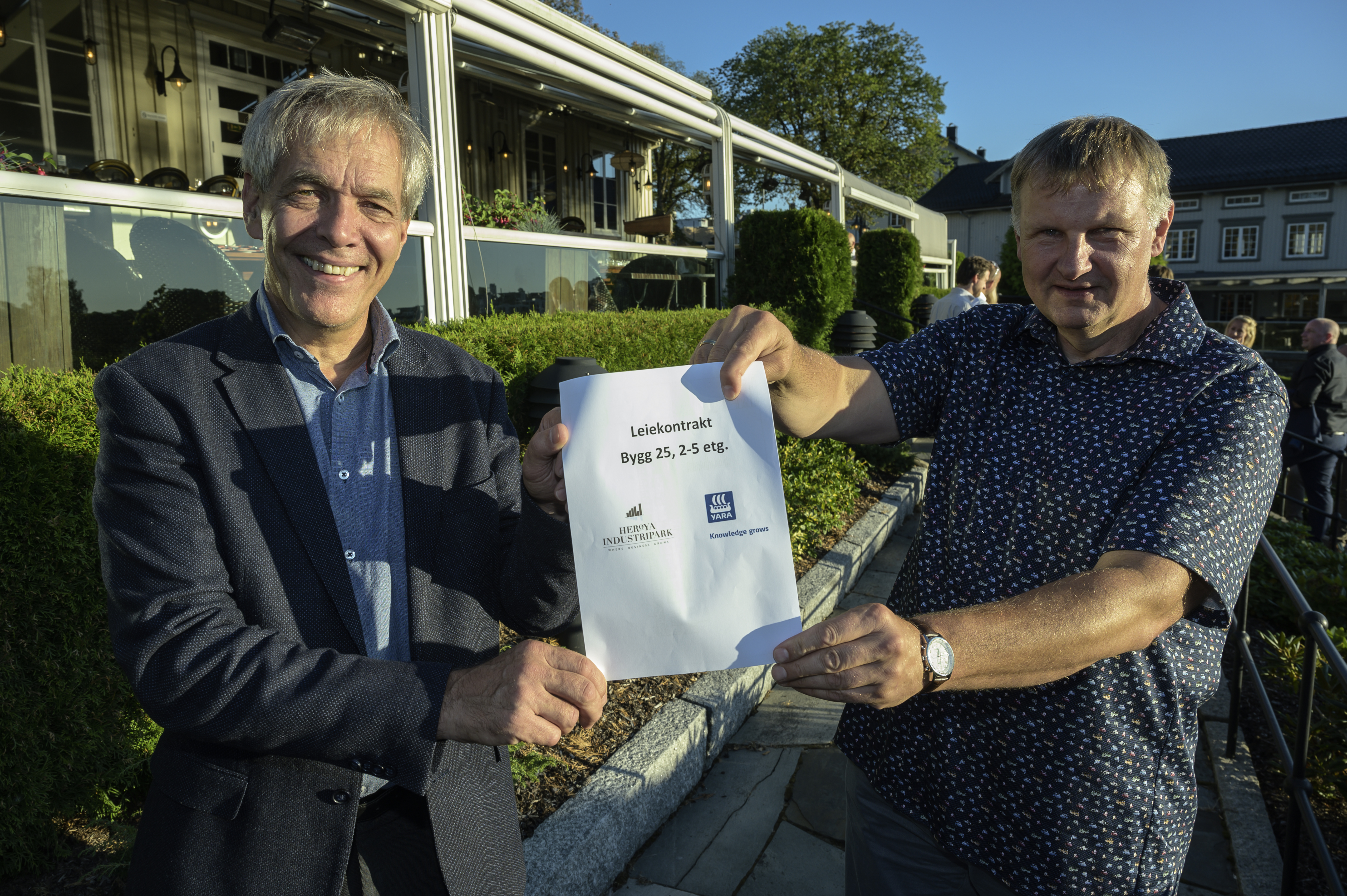 to menn står ute i restauranthage og holder et A4-ark, avtale, sammen