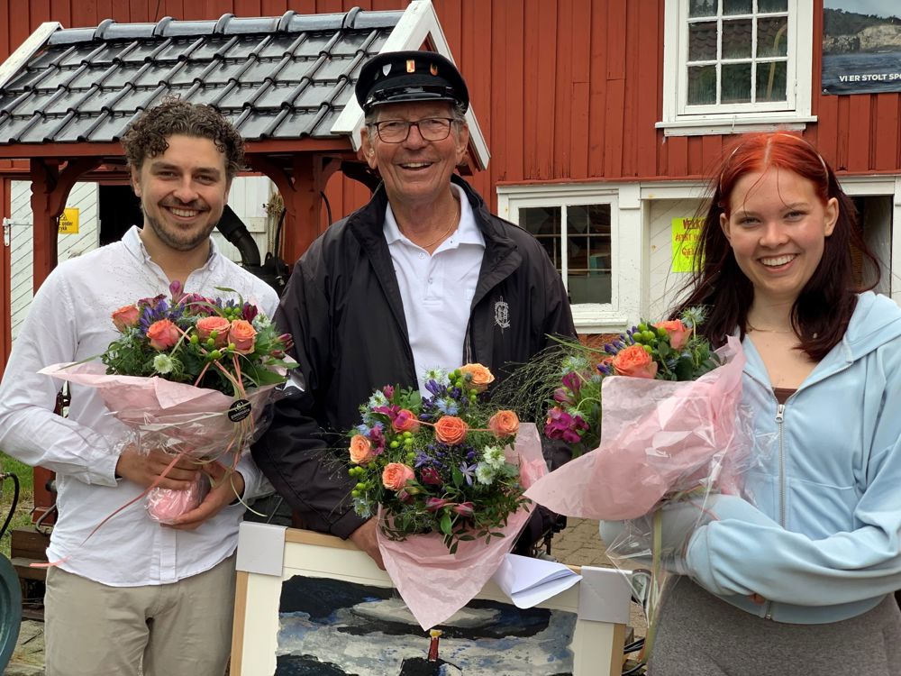 senior i midten og to ungdommer på hver sin side, poserer, blomsterbuketter, rød trebygning i bakgrunnen.