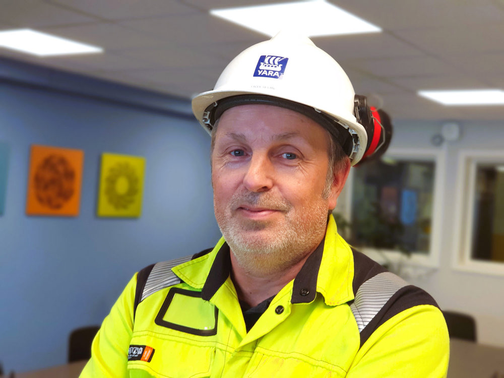 portrait of man, wearing yellow jacket and white helmet, in a meeting room.