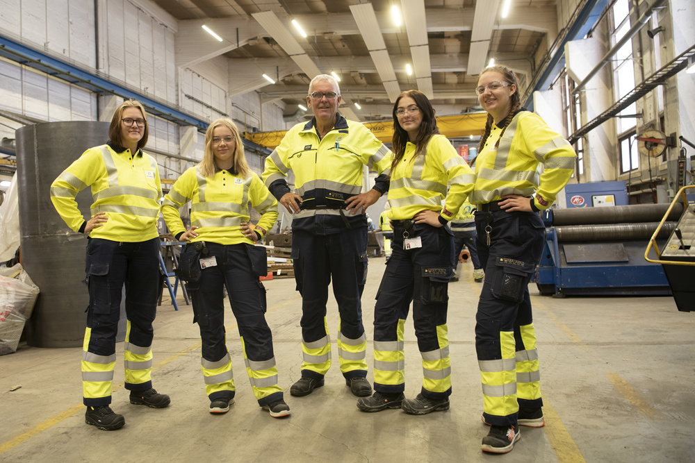 four young women stand in a workshop with senior man in the middle