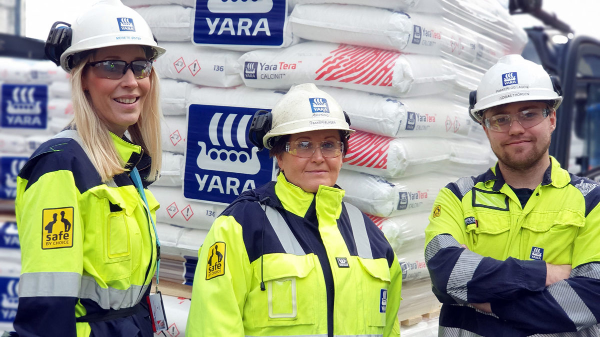 three persons, posing, work clothes, helmets, bags of fertiliser on a pallet