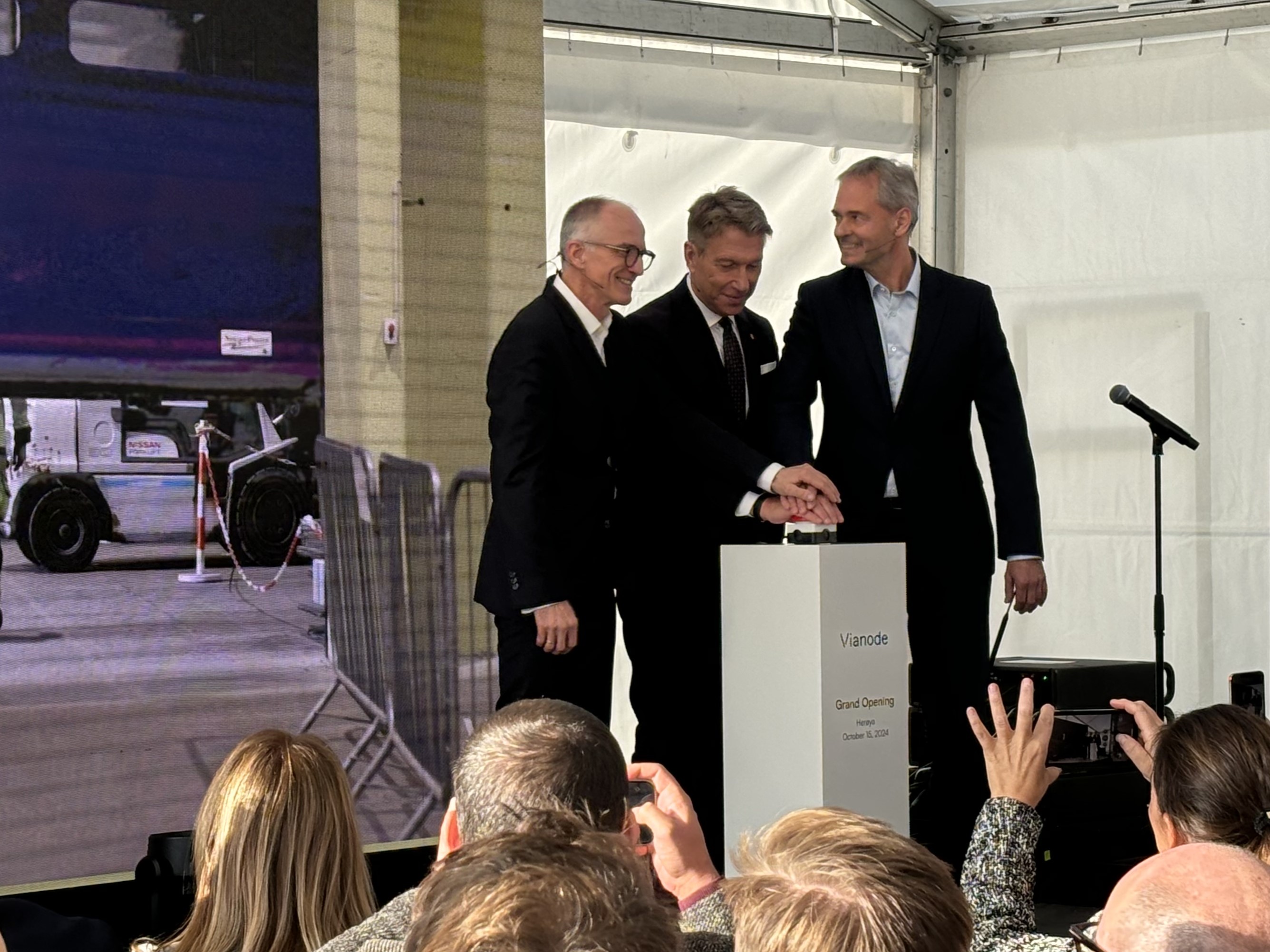 three men on stage, all with one hand each on a big red buzzer, opening sceremony