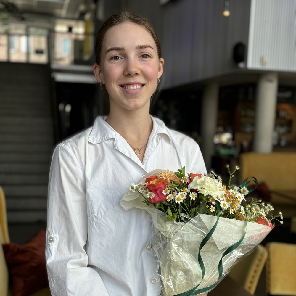 portrett av ung kvinne i hvit skjorte, poserer, holder blomsterbukett.