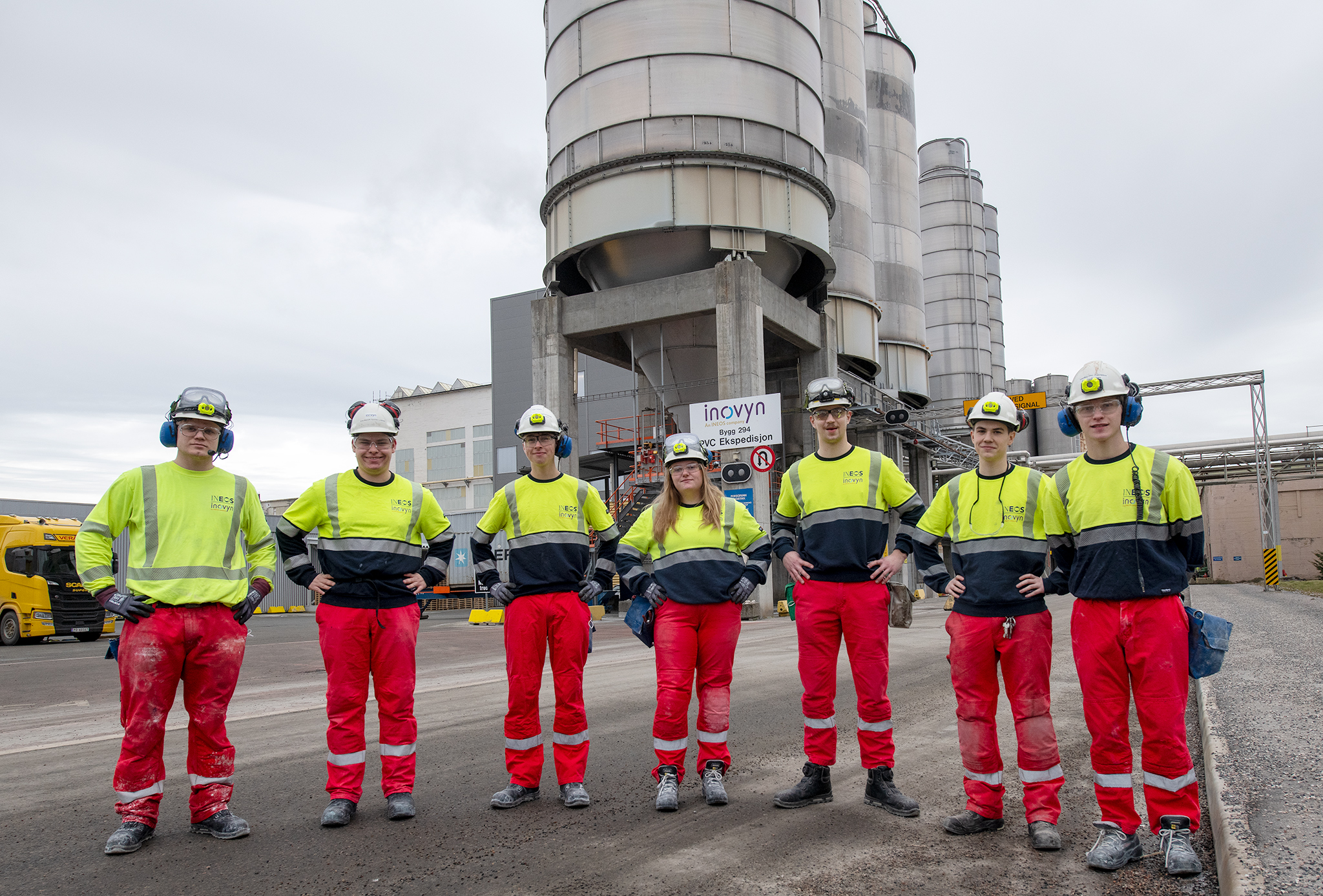 seven young apprentices, working clothes, outdoors in front of production plant