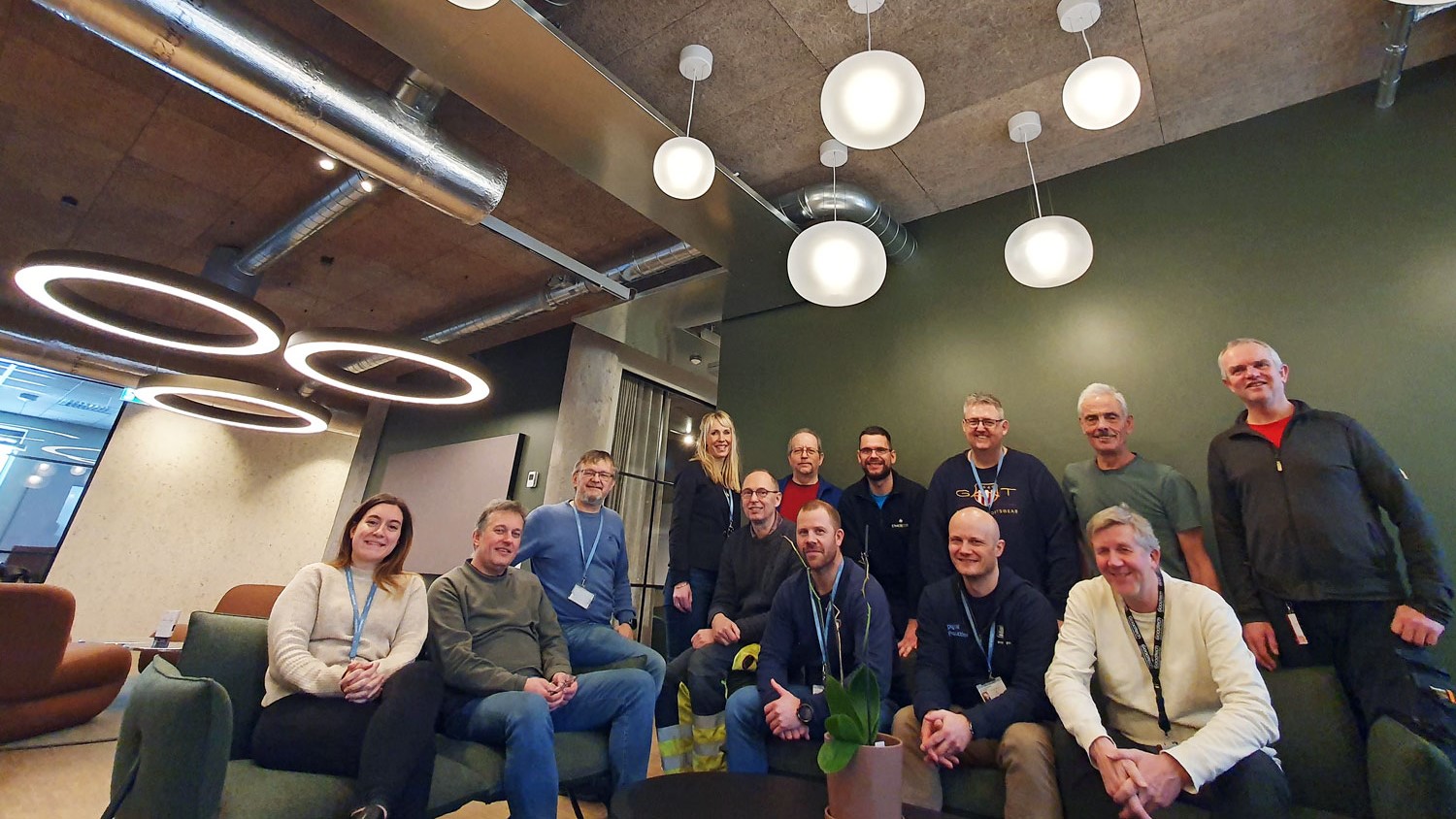 big group of colleagues standing and sitting in sofa and chairs in an office environment.