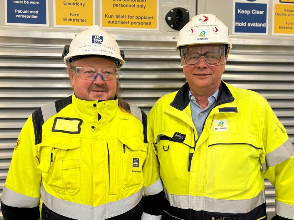 two men posing, with their back to a door for technical room.