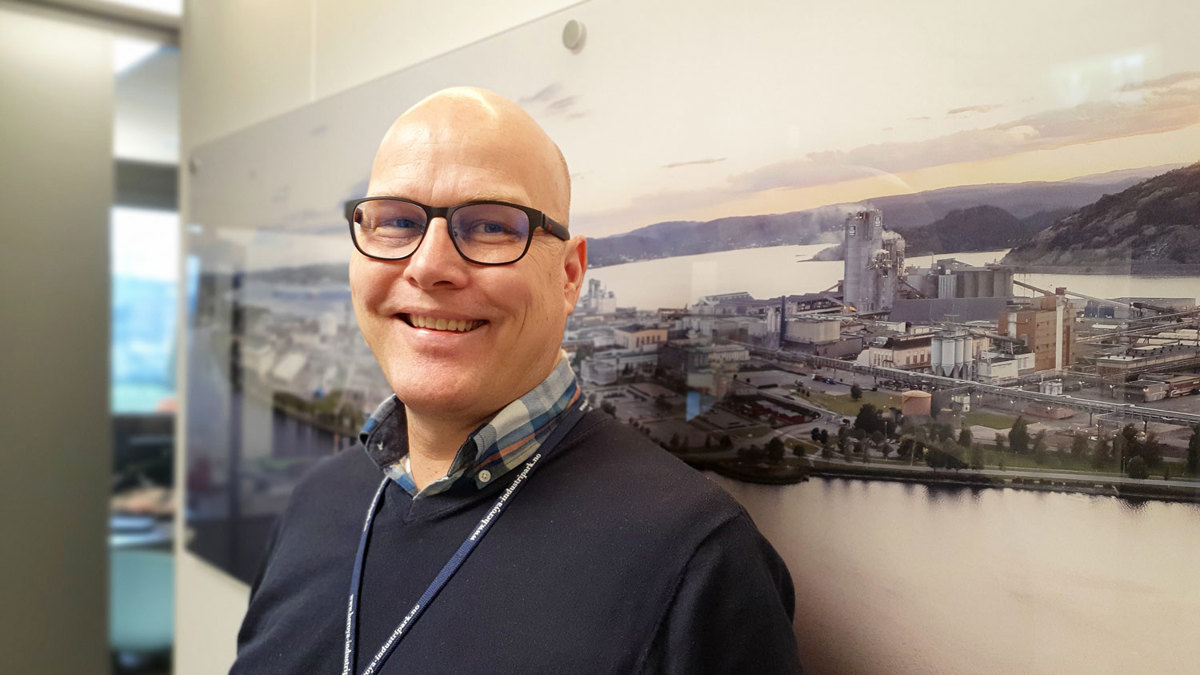 portrett av mann, briller, foran foto på vegg