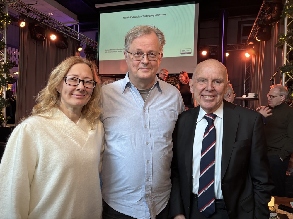 three people standing together, big screen on stage in background.