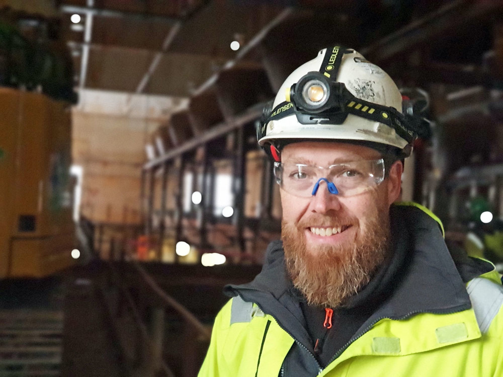 man with beard wearing protective glasses and white helmet in a dark big hall