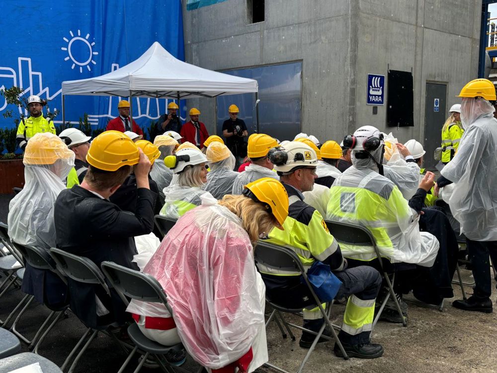 audience and guest sitting on fold-up chair, yellow helmets and thin rain wear.