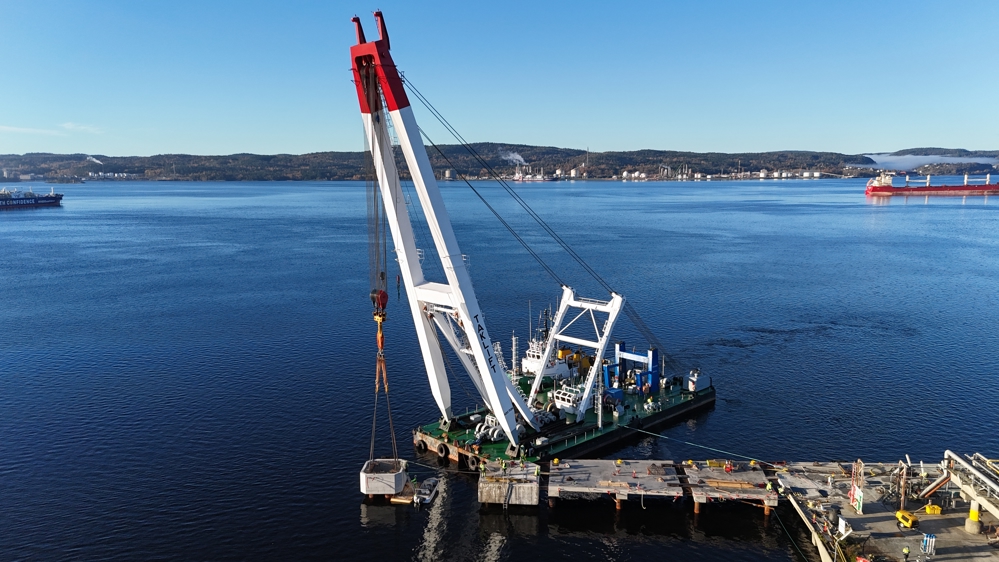 Large crane ship, unloading concrete elements, sea, quay, vessel in background.