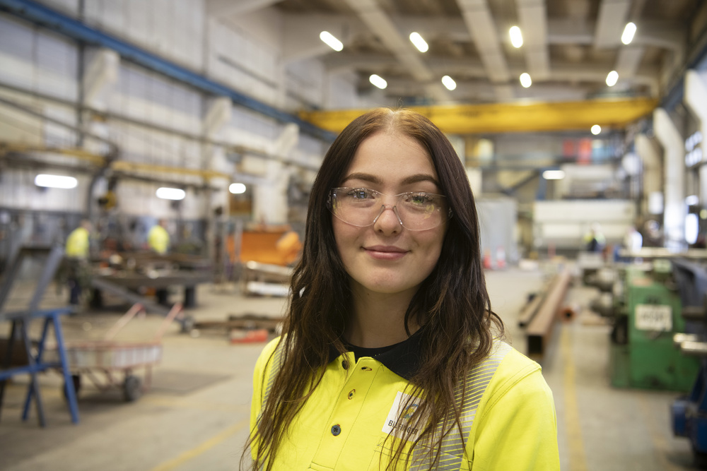 young female apprentice long dark hair standing in workshop hall