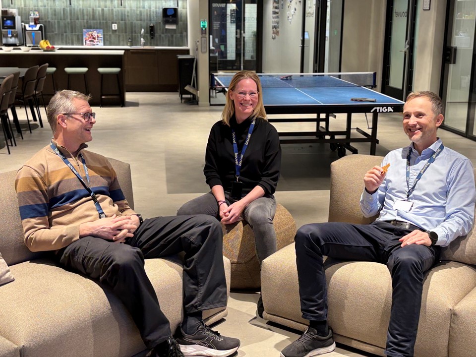three persons sitting in a lounge area, table tennis table in background, office environment, social zone.