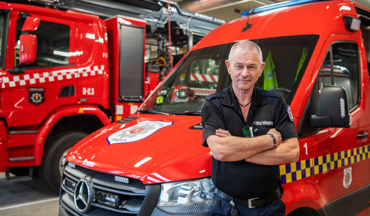 man, posing, arms crossed, leaning into a red fire and rescue vehicle