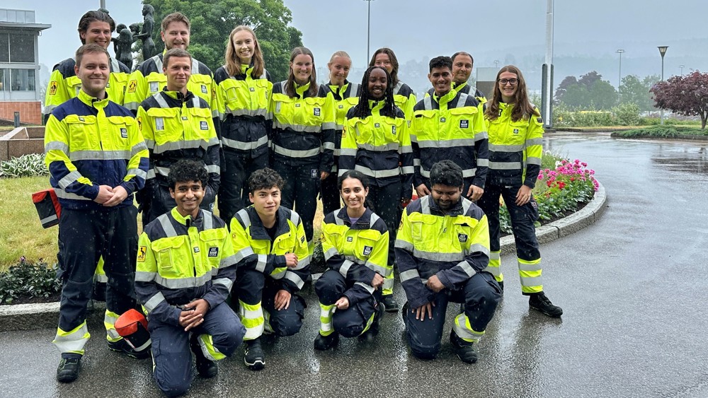 group of students standing in three rows, front row kneeling, posing, yellow and blue working clothes, outdoors, park, green area, raining.