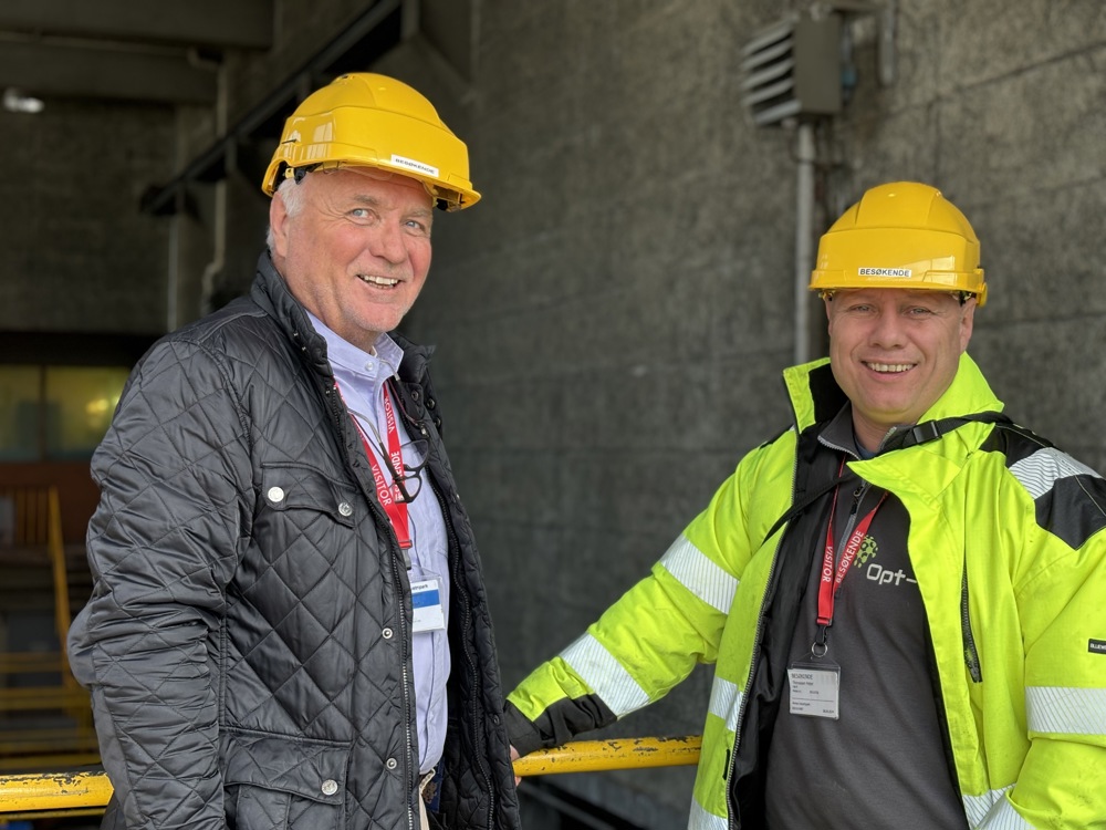 two men, yellow helmets, posing, leaning on to yellow rails, grey concrete wall behind them