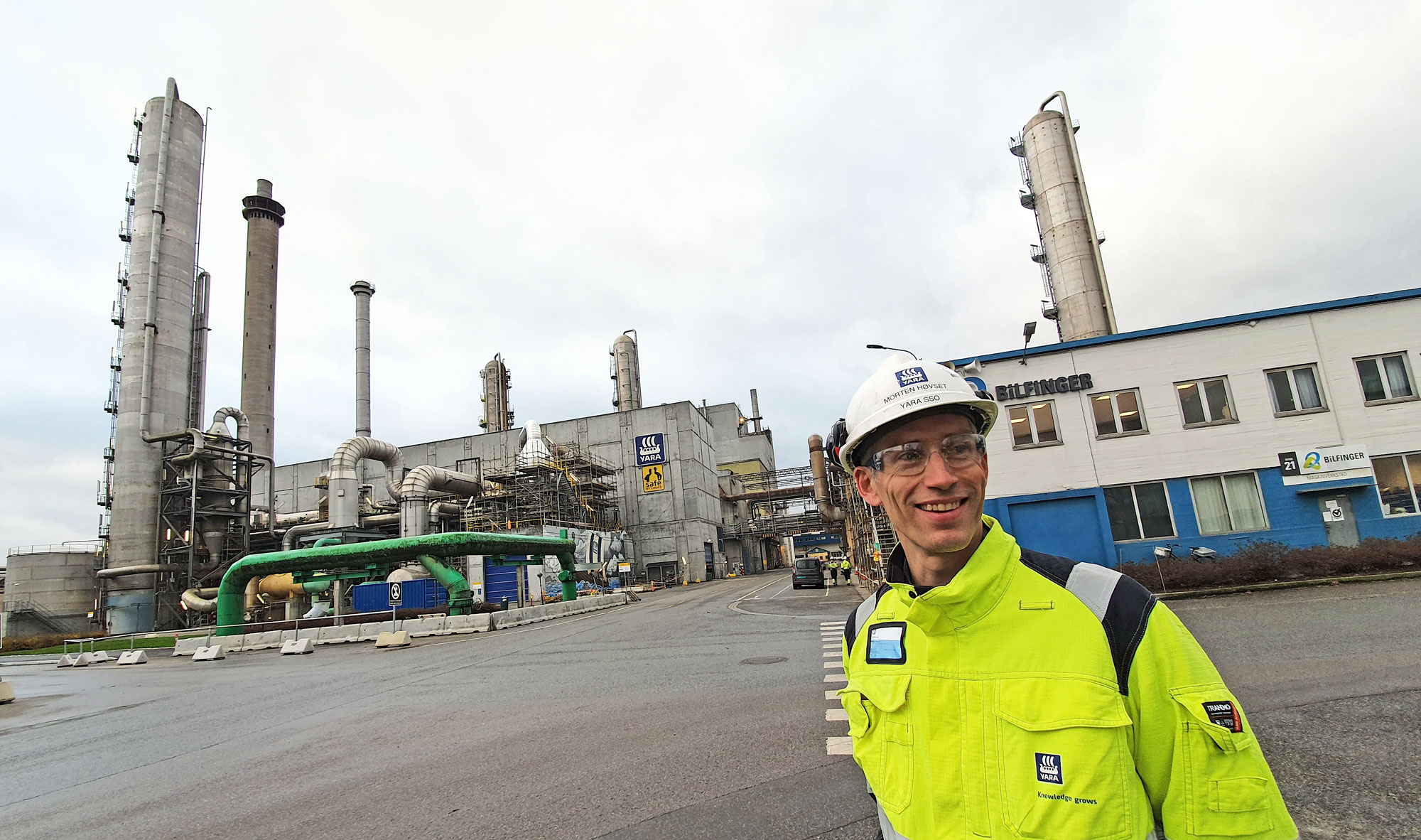 mann står i gatekryss i industripark, fabrikkpiper bak