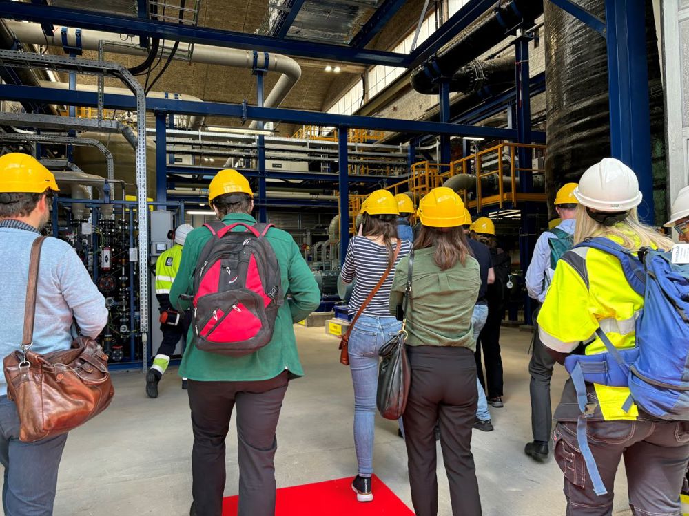 A lot of press, wearing yellow helmets, on their way in to the plant.