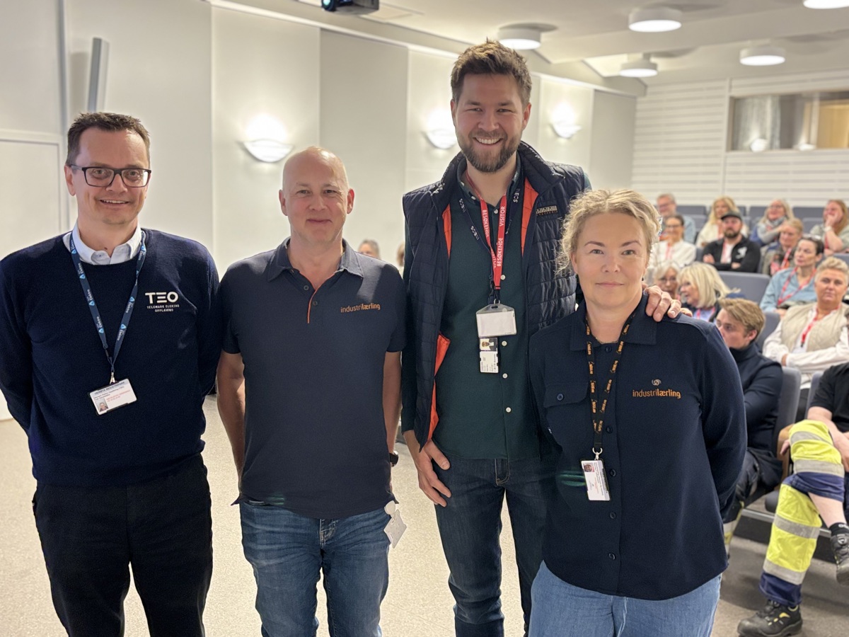 fire personer foran fullsatt auditorium i bakgrunnen