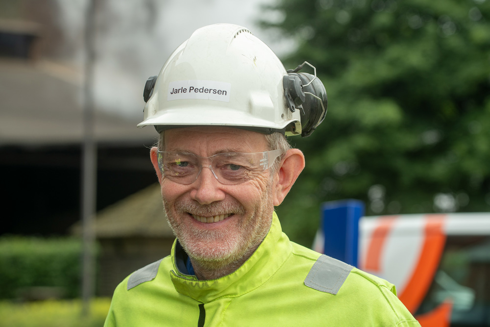 portrait of man, short beard, goggles, white helmet and yellow buttened jacket, outside factory area.