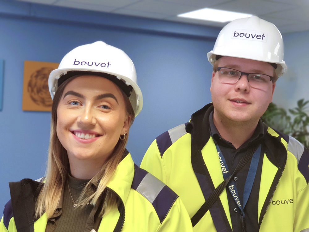 portrait of smiling young woman and young man with glasses, yellow jackets, white helmets, standing