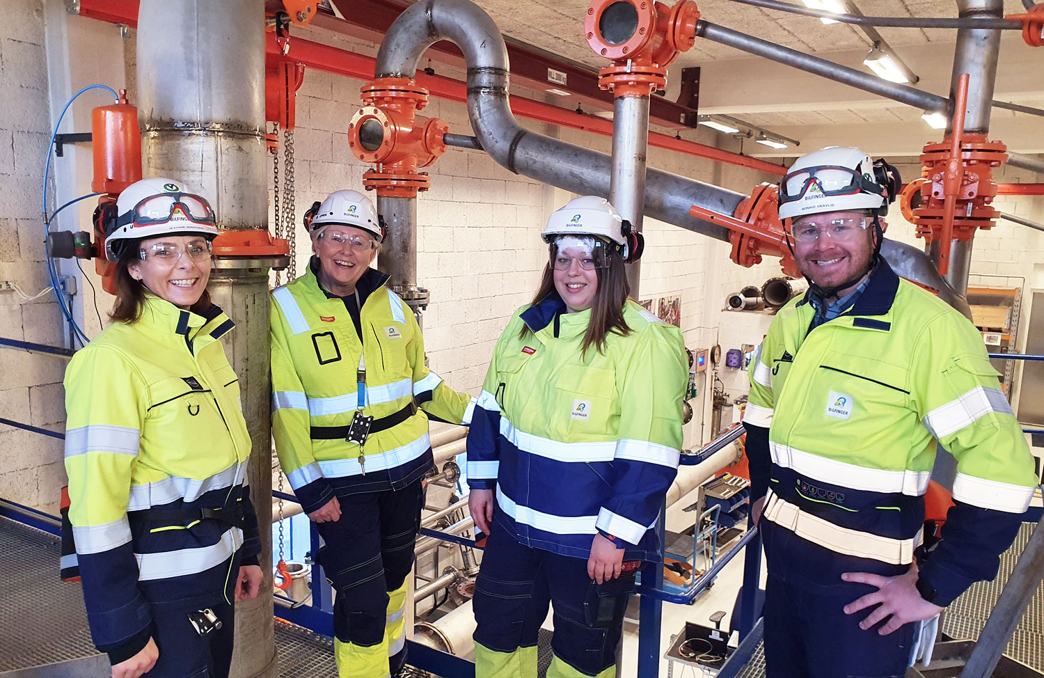 four people standing in a production hall, posing, working clothes