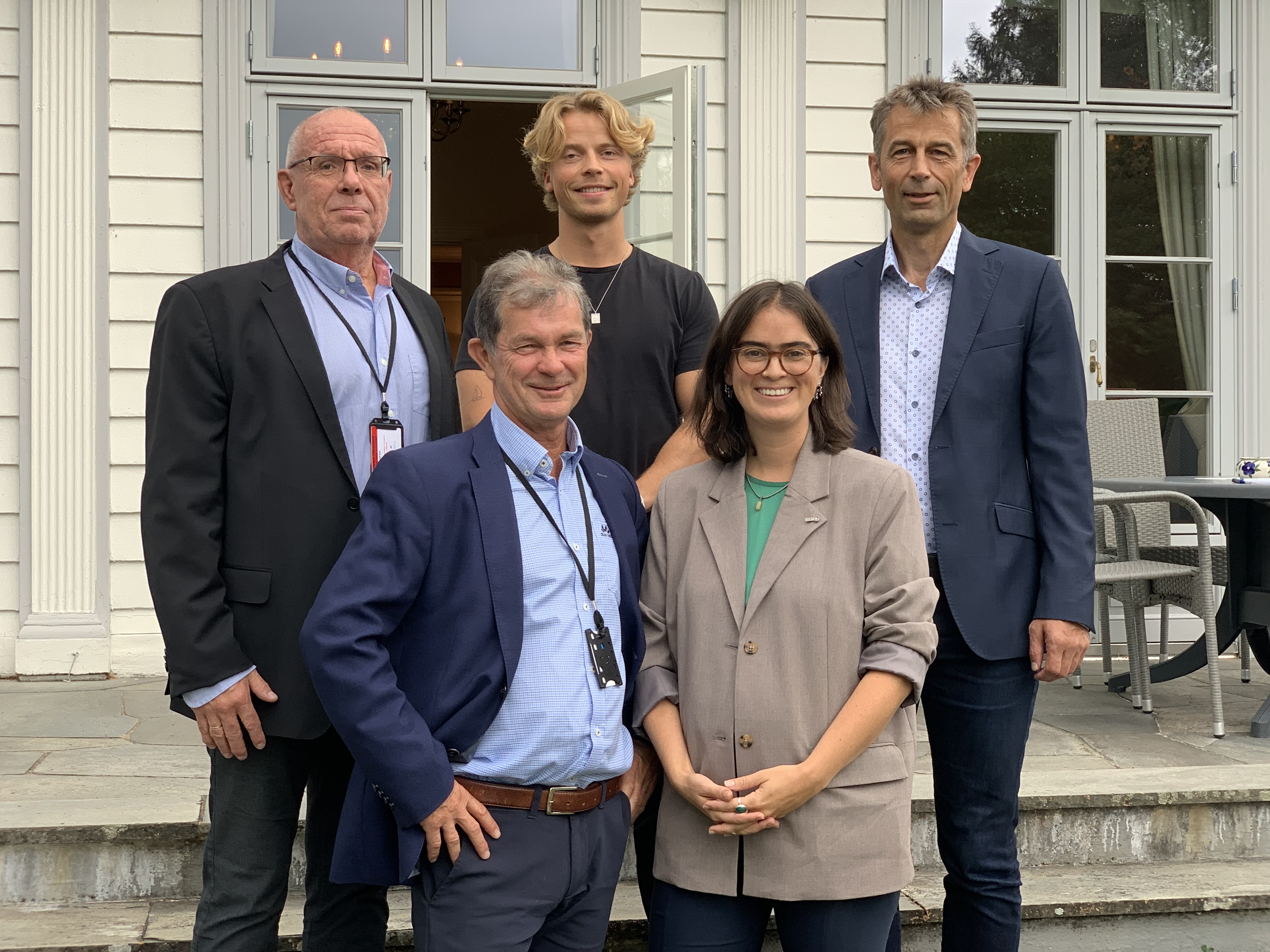 portrett av fem personer, de står på en trapp foran representasjonsbygg, gruppe, en kvinne i lys blaser, fire menn i dress.