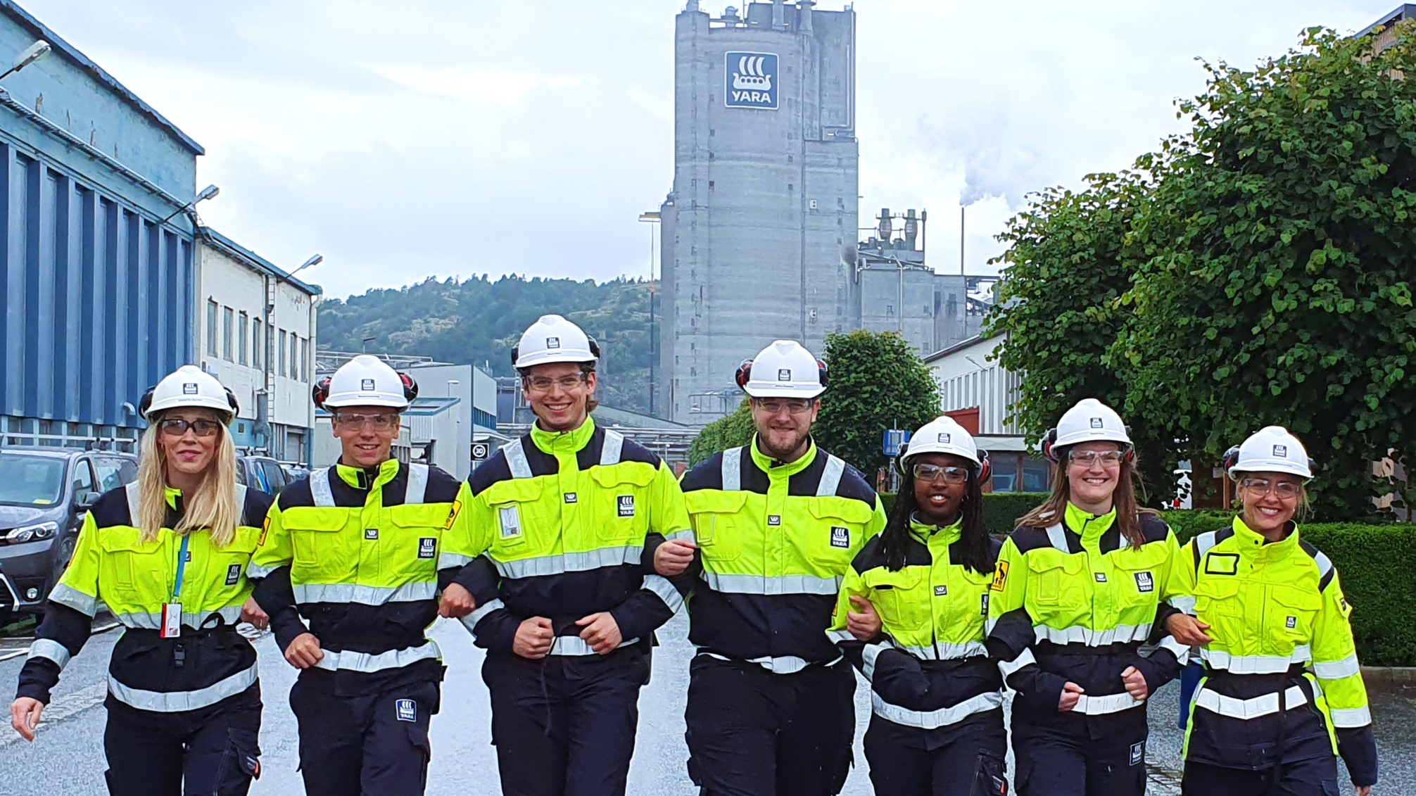 seven persons, posing, wearing yellow and blue work clothes, helmets, walking towards the camera