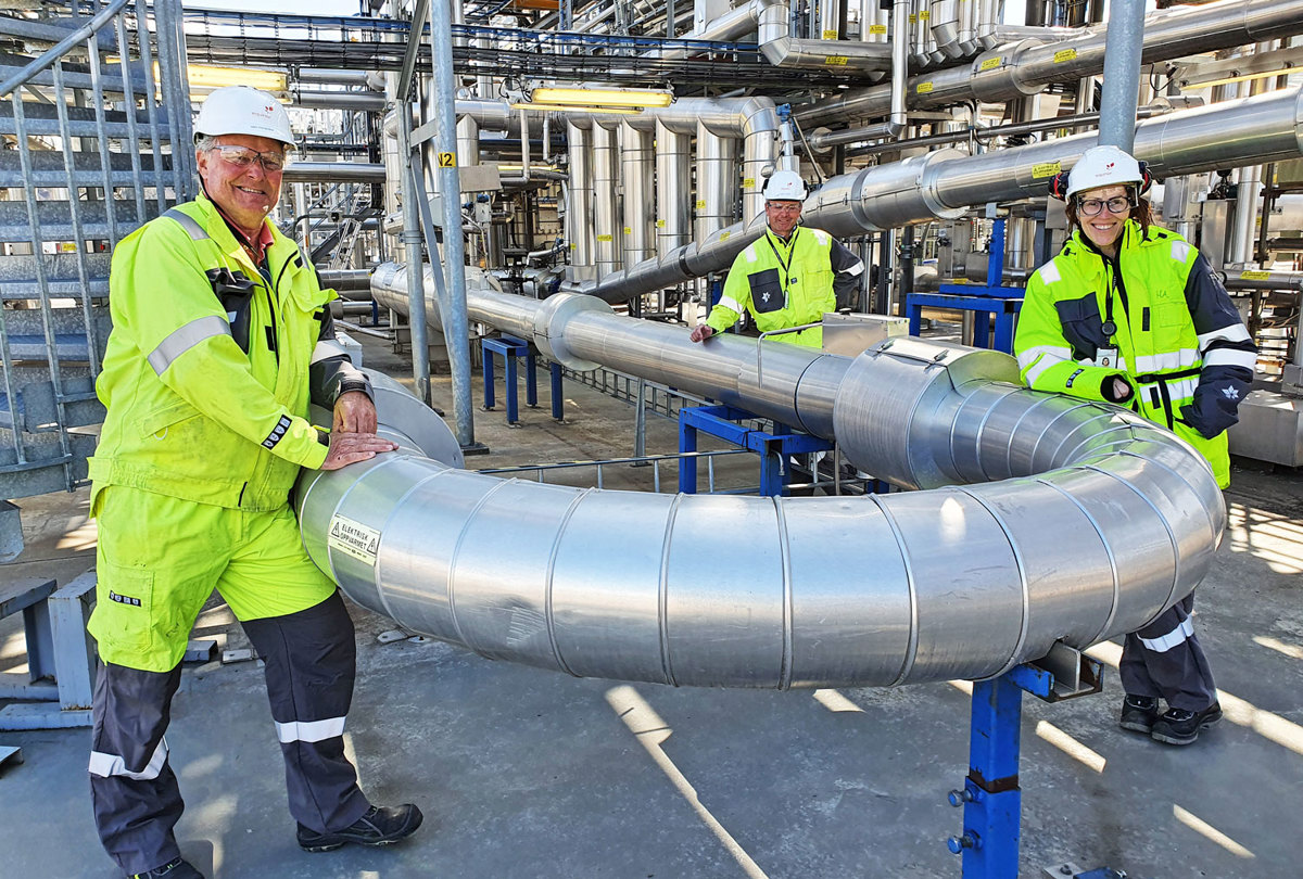 tre personer, poserer, lener seg på et stålrør, i et flerfaseanlegg