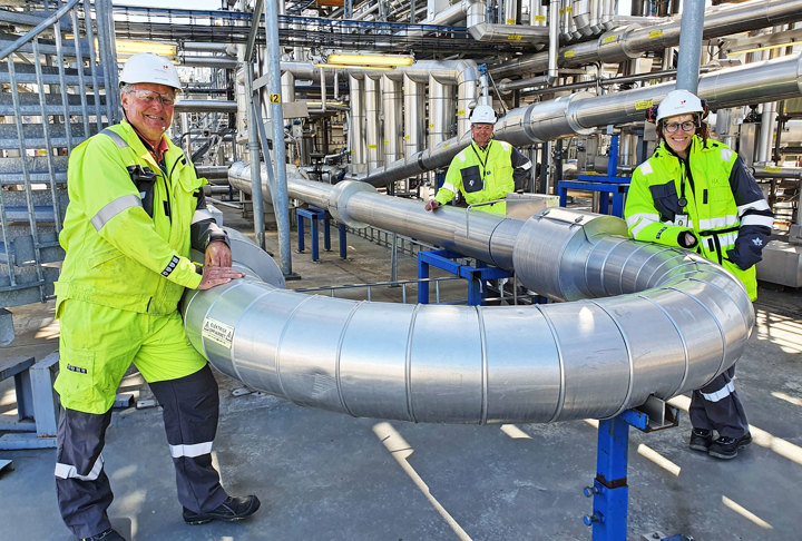 tre personer, poserer, lener seg på et stålrør, i et flerfaseanlegg